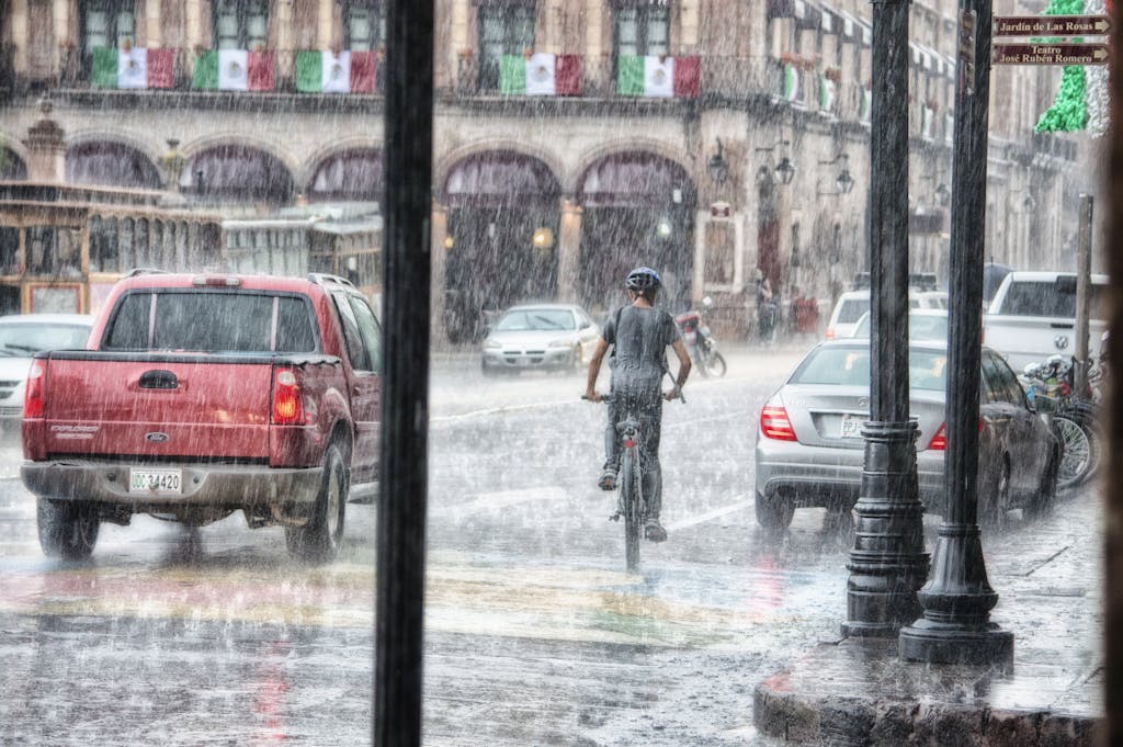 Imagen actual: A cyclist rides through heavy rain in Morelia's urban street scene, Mexico.