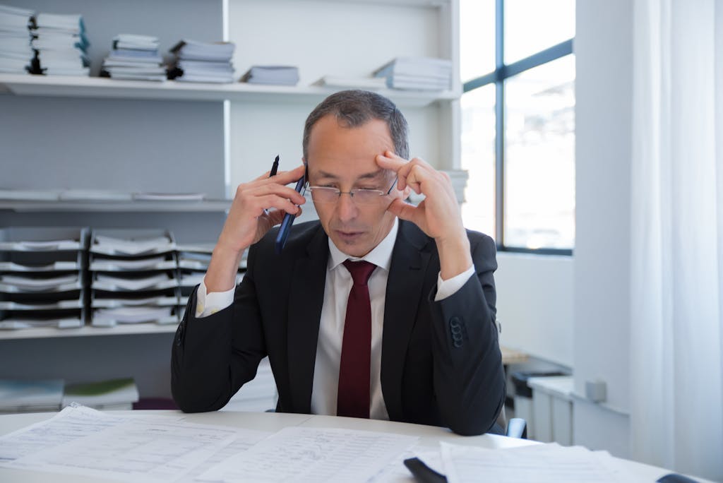 Imagen actual: Businessman in a black suit stressed over documents in a bright office setting.