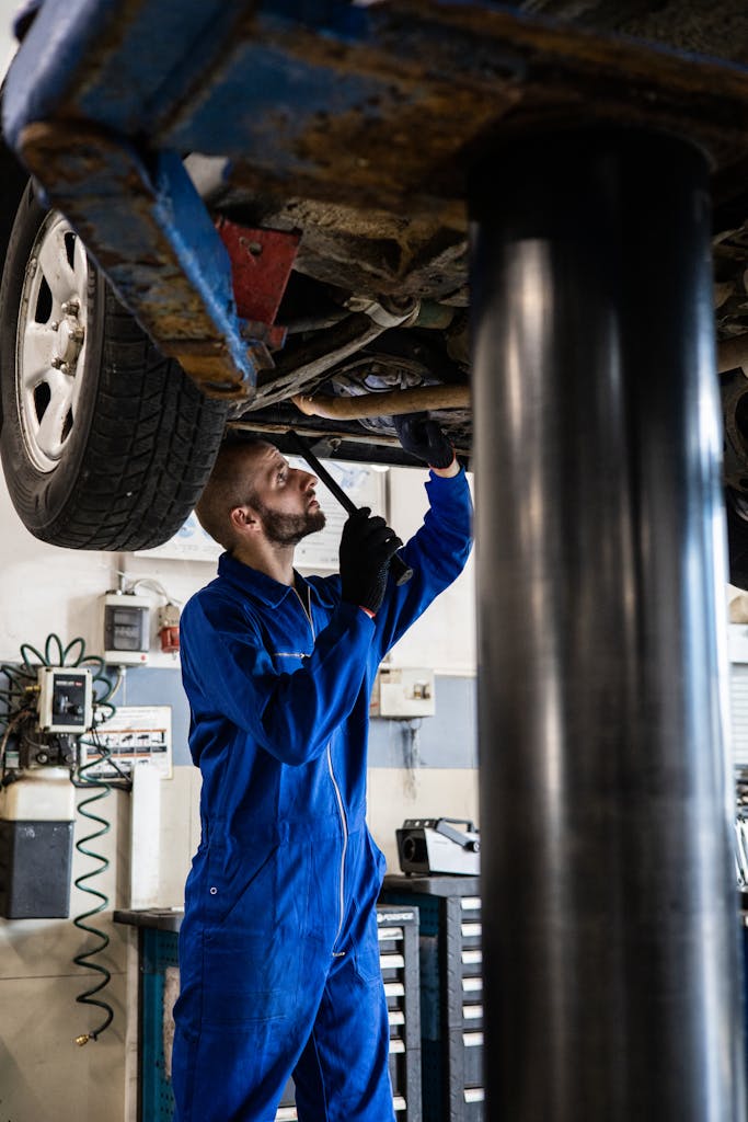 Imagen actual: Mechanic in blue coveralls inspecting car undercarriage on hydraulic lift.