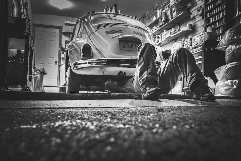 Imagen actual: Mechanic working beneath a classic Volkswagen Beetle in a vintage garage setting.