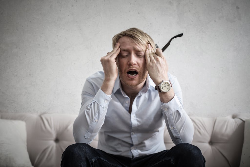 Imagen actual: Stressed man sitting on couch, feeling overwhelmed and frustrated, expressing mental strain.