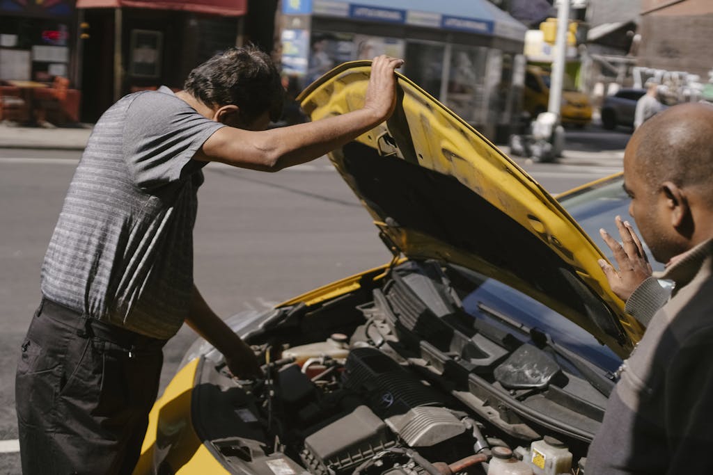 Imagen actual: Two mechanics checking engine issues with a car on a busy urban street.