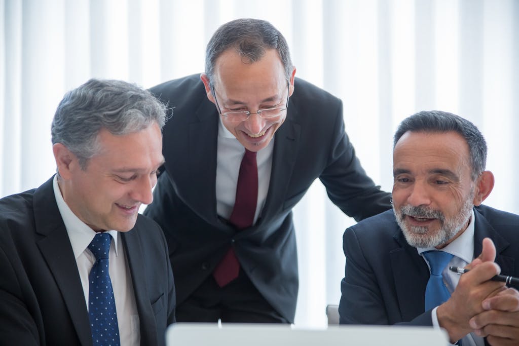 Imagen actual: Three businessmen in suits engaging in teamwork indoors with smiles.