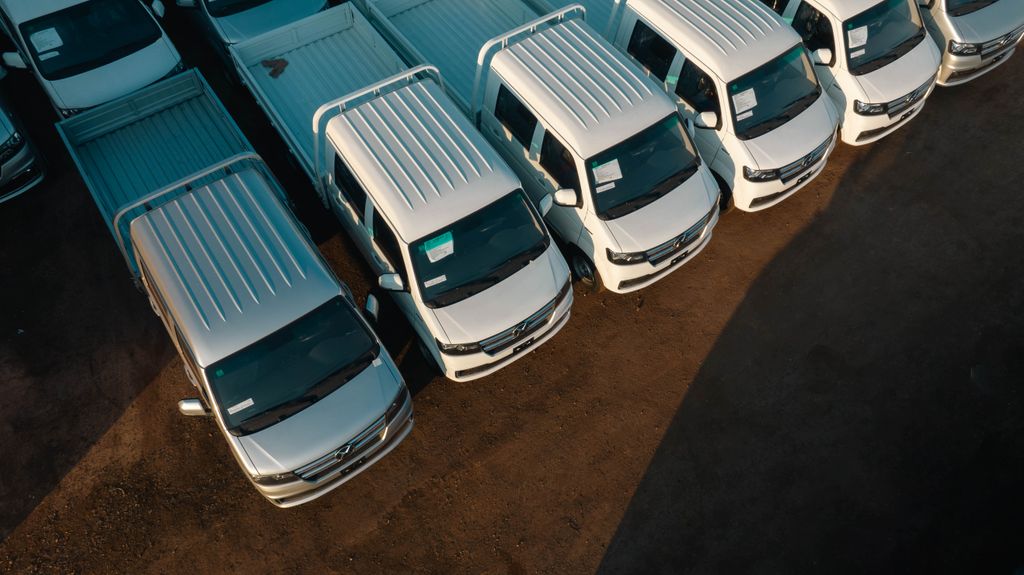 Imagen actual: Aerial view of white pickup trucks aligned neatly in a parking lot. High contrast lighting.